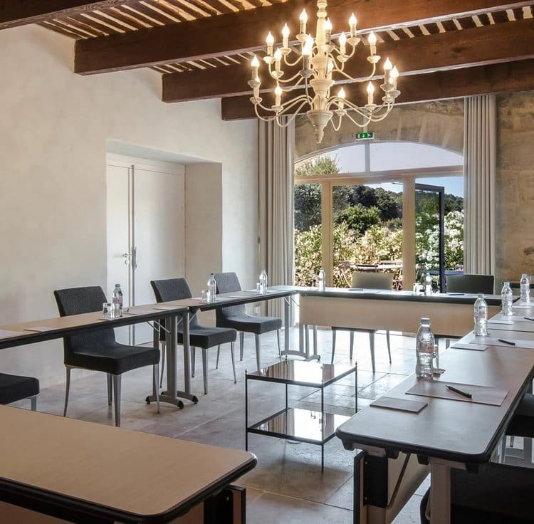 Salle de réunion avec murs en pierres apparentes, grande table moderne, et lumière naturelle filtrant à travers de grandes fenêtres.