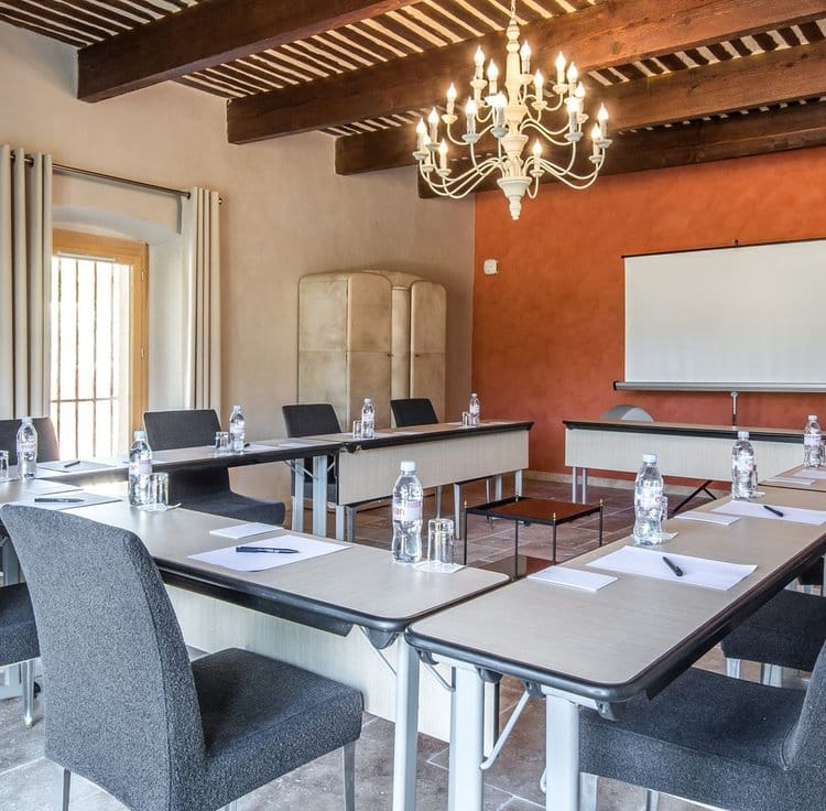 Salle de réunion avec murs en pierres apparentes, grande table moderne, et lumière naturelle filtrant à travers de grandes fenêtres.