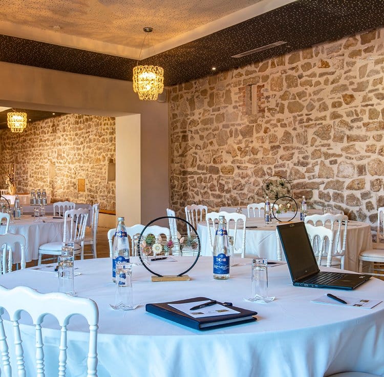 Salle de séminaire avec murs en pierre rustique, mobilier contemporain, et éclairage chaleureux par des lustres élégants.
