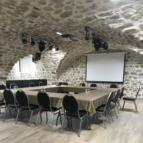 Salle de réunion en pierre avec écran et chaises au Domaine des Ranchisses